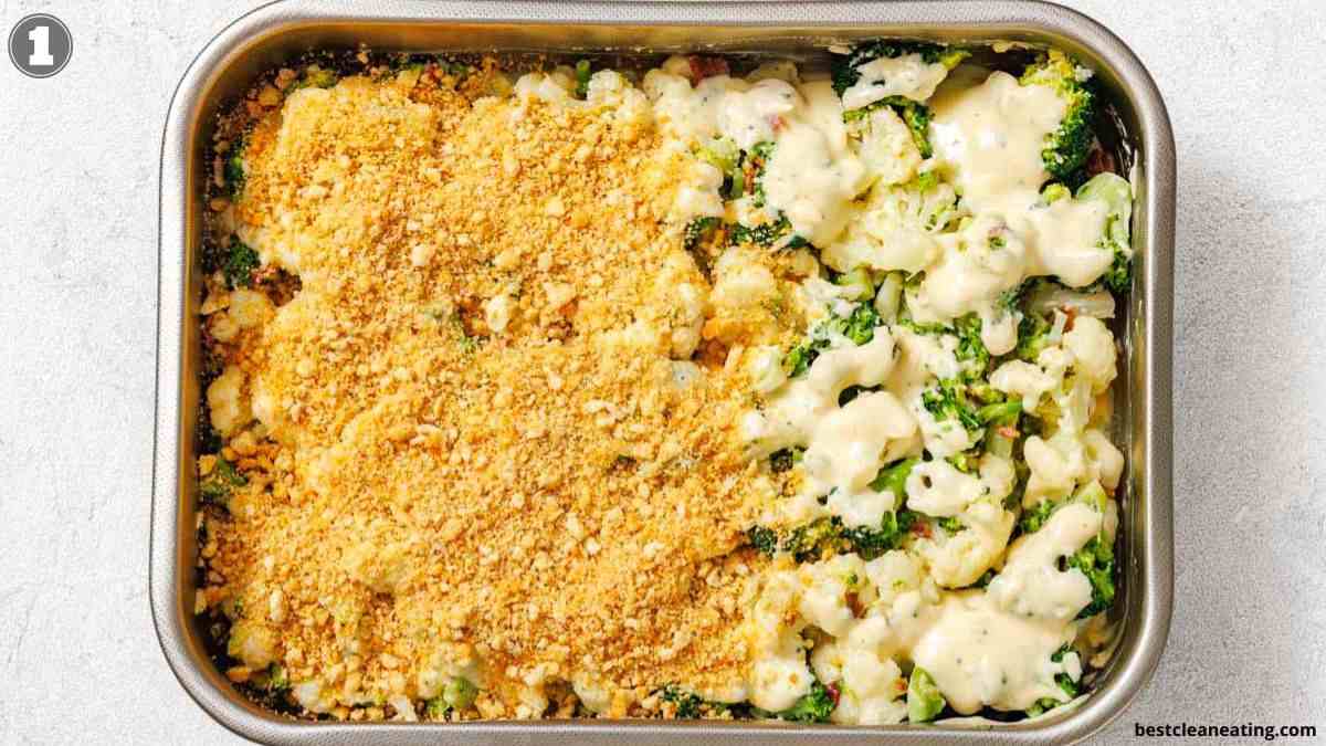 A baking dish containing broccoli and cauliflower casserole, half covered with a breadcrumb topping and half with cheese sauce, on a light surface.