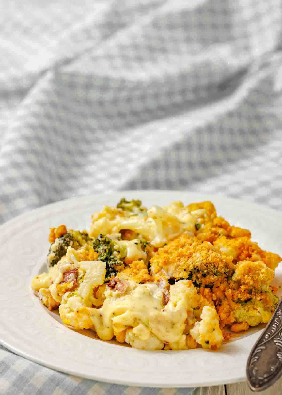 A serving of broccoli casserole with a cheesy, golden-brown topping on a white plate, set against a light, textured background.