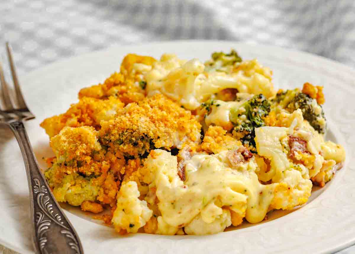 A plate of baked broccoli and cauliflower bake topped with melted cheese and breadcrumbs, served with a fork.