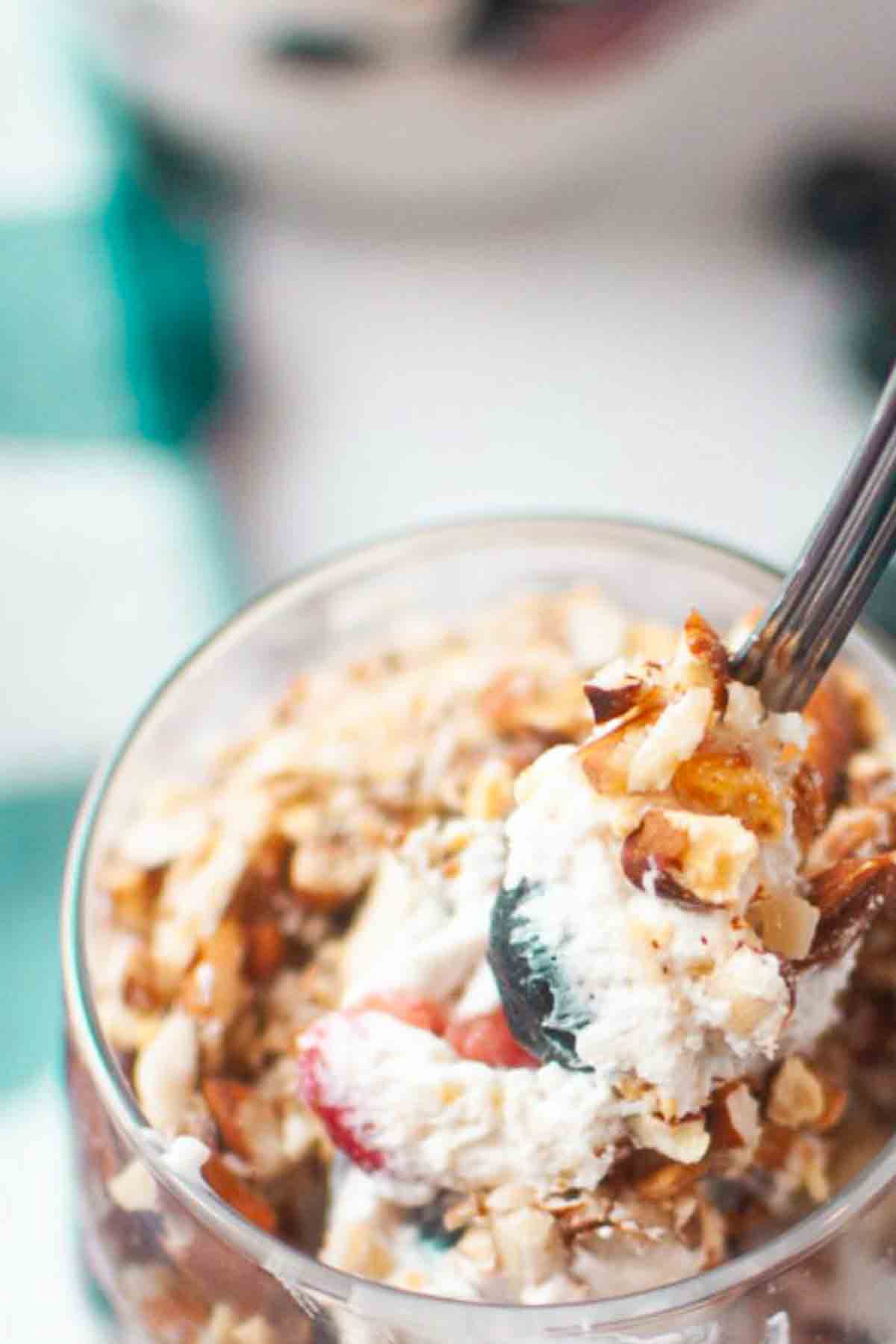 A close-up of a glass filled with yogurt, granola, and berries; a spoon is lifting a portion from the glass.