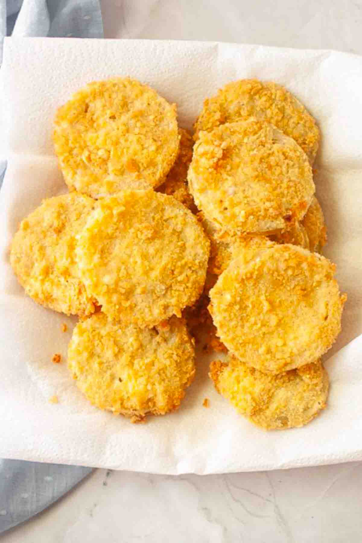 A plate lined with paper towels holds several golden-brown, breaded and fried round slices, likely fried green tomatoes.