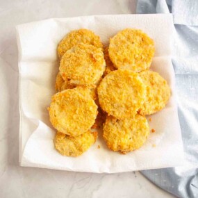 A plate lined with paper towels holds several pieces of golden brown fried food, arranged in a single layer on a light surface.