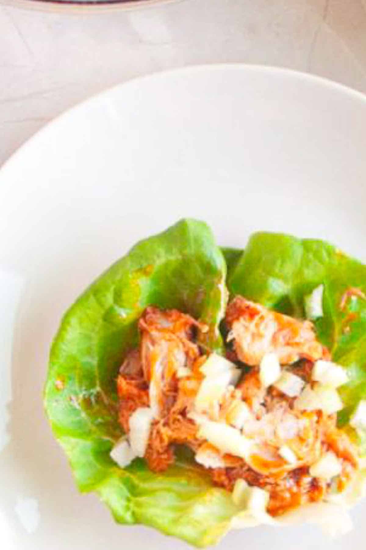 A lettuce leaf topped with shredded meat and diced onions on a white plate.