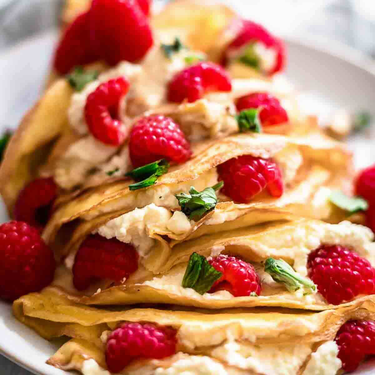Fresh raspberry cream cheese crepes on white plate.