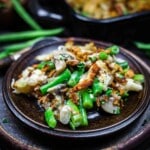 A plate of green bean casserole topped with crispy fried onions and garnished with chopped herbs.