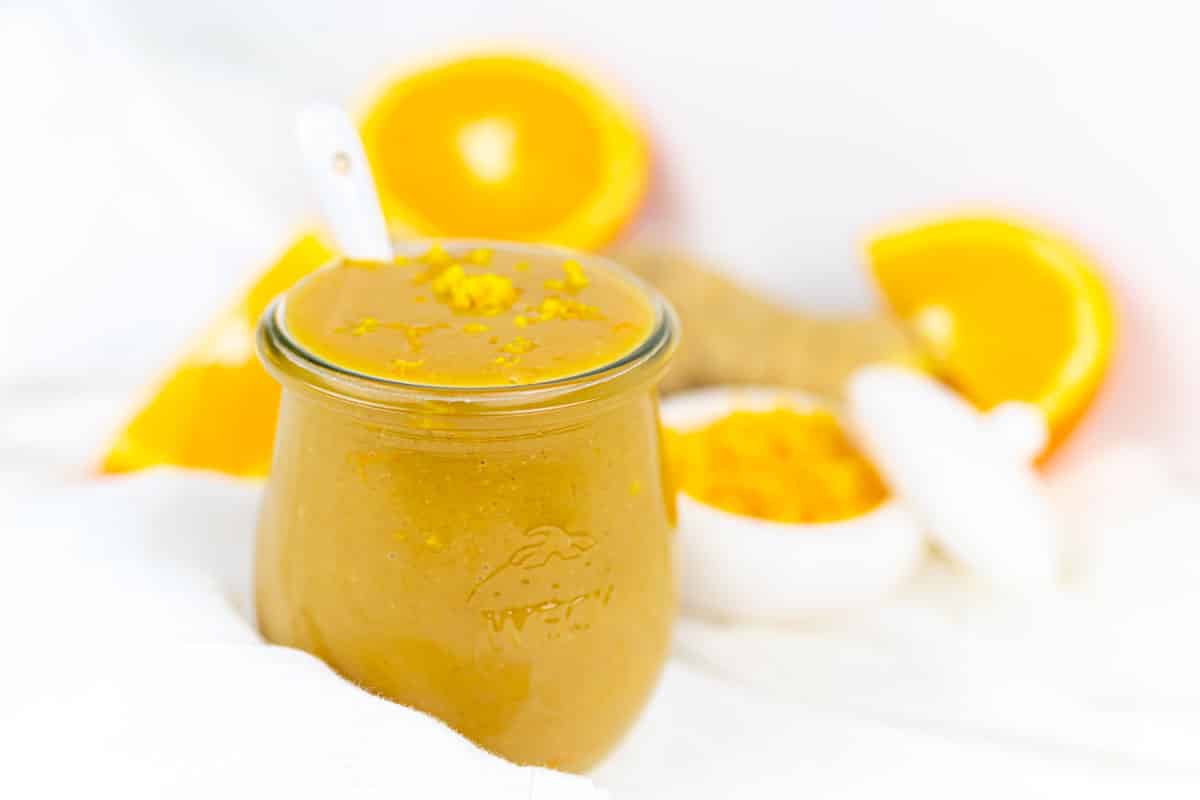 Jar of orange sauce with oranges background.