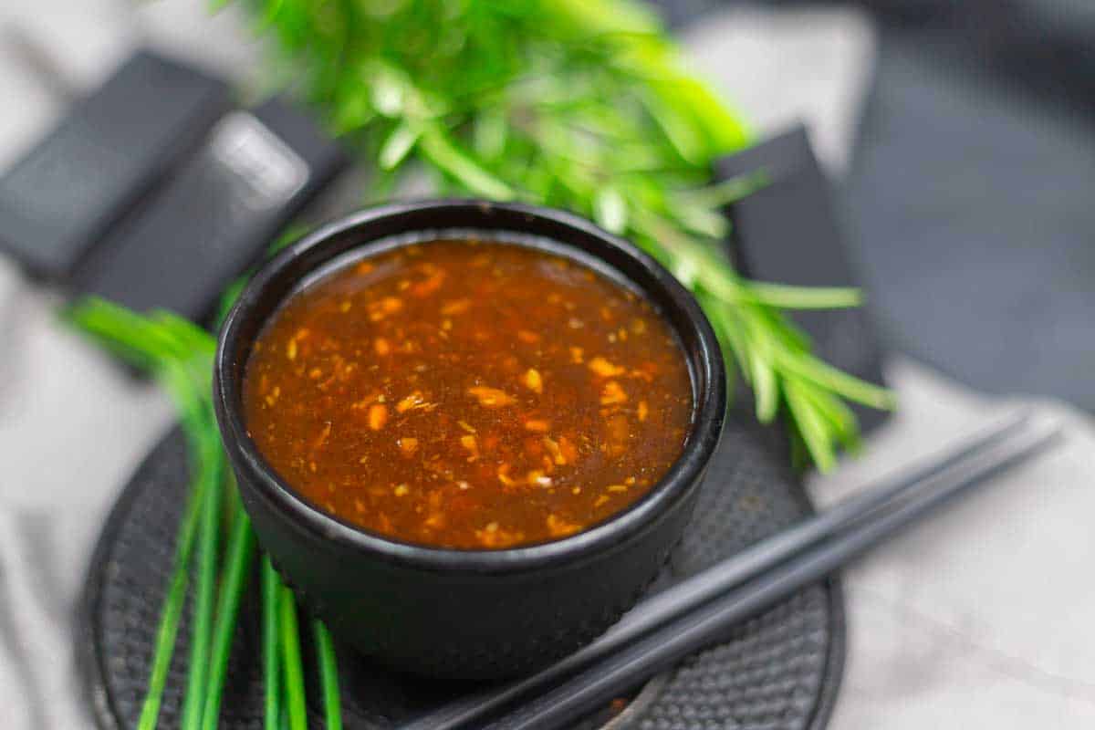 A black bowl filled with a thick, Korean BBQ sauce, with green herbs and black chopsticks nearby.