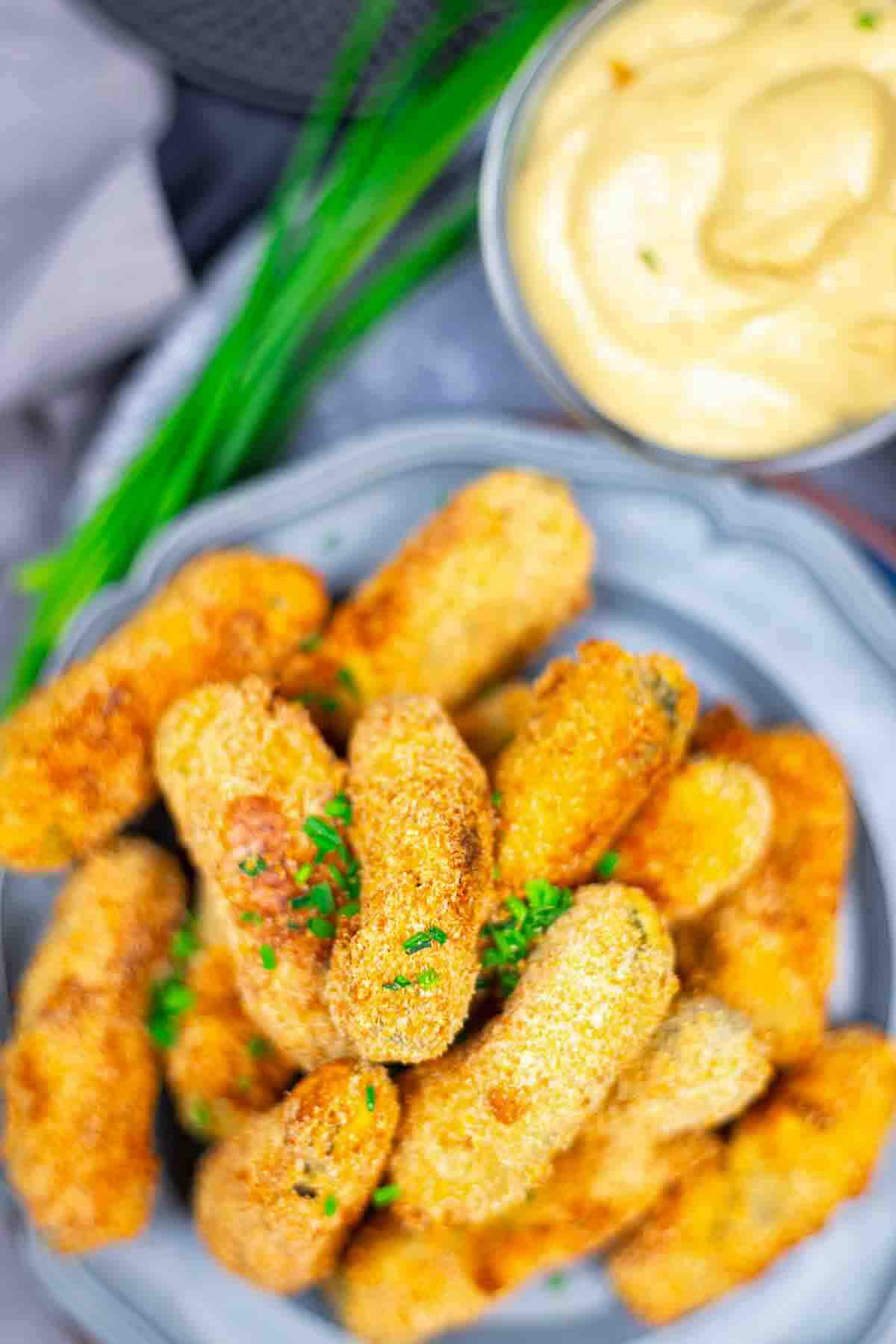 Breaded pickled gherkins served beside creamy sauce.