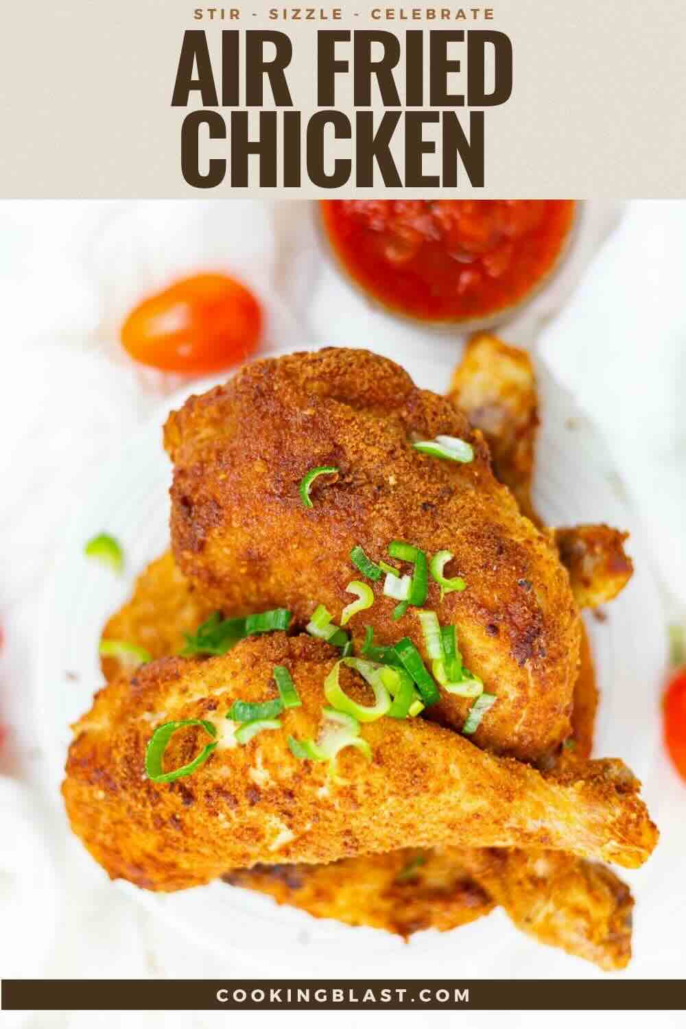 A plate of air fried chicken drumsticks garnished with chopped green onions, served with cherry tomatoes and a small dish of sauce.