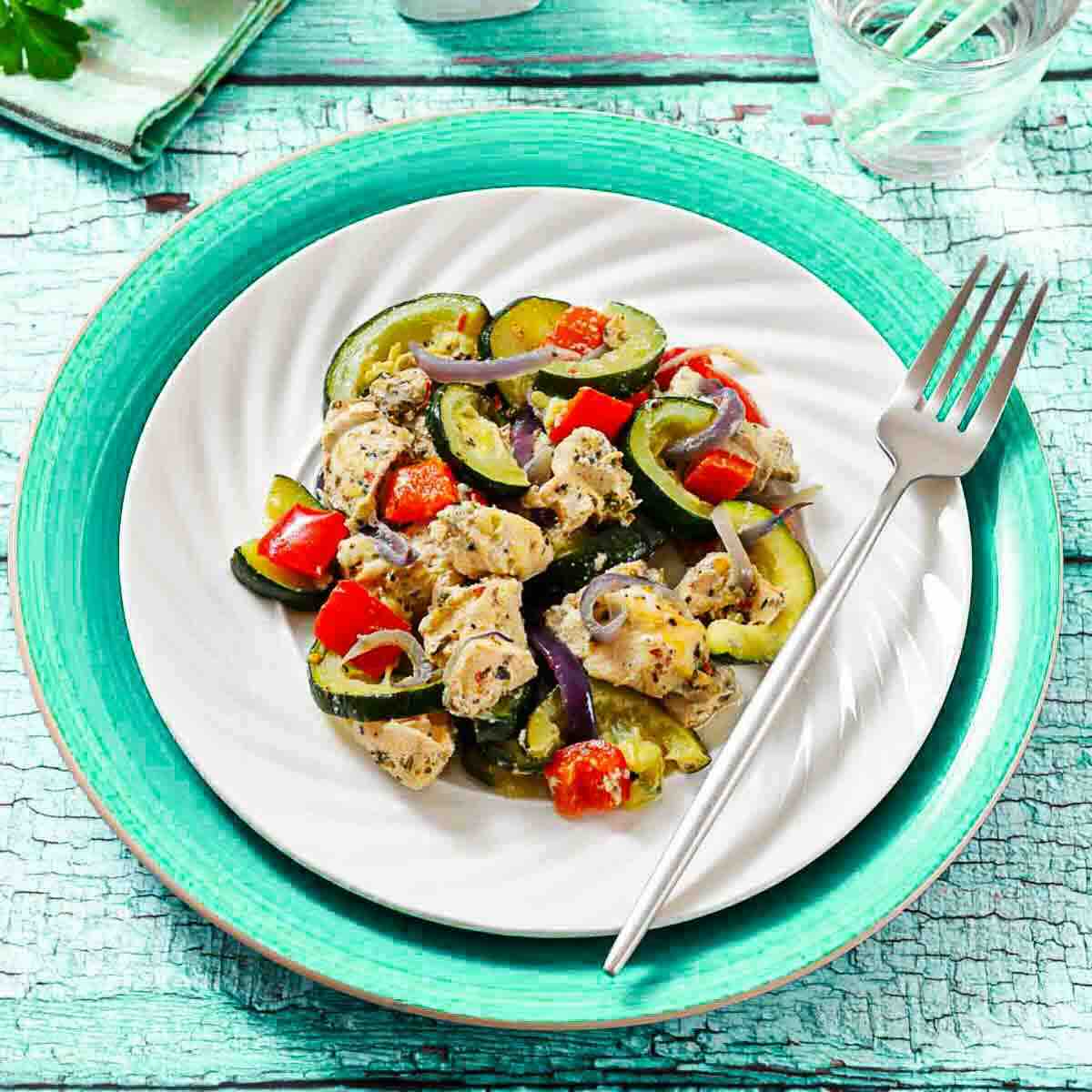 A plate of chicken and vegetable stir-fry featuring zucchini, red bell pepper, and red onion, served on a white plate with a fork.