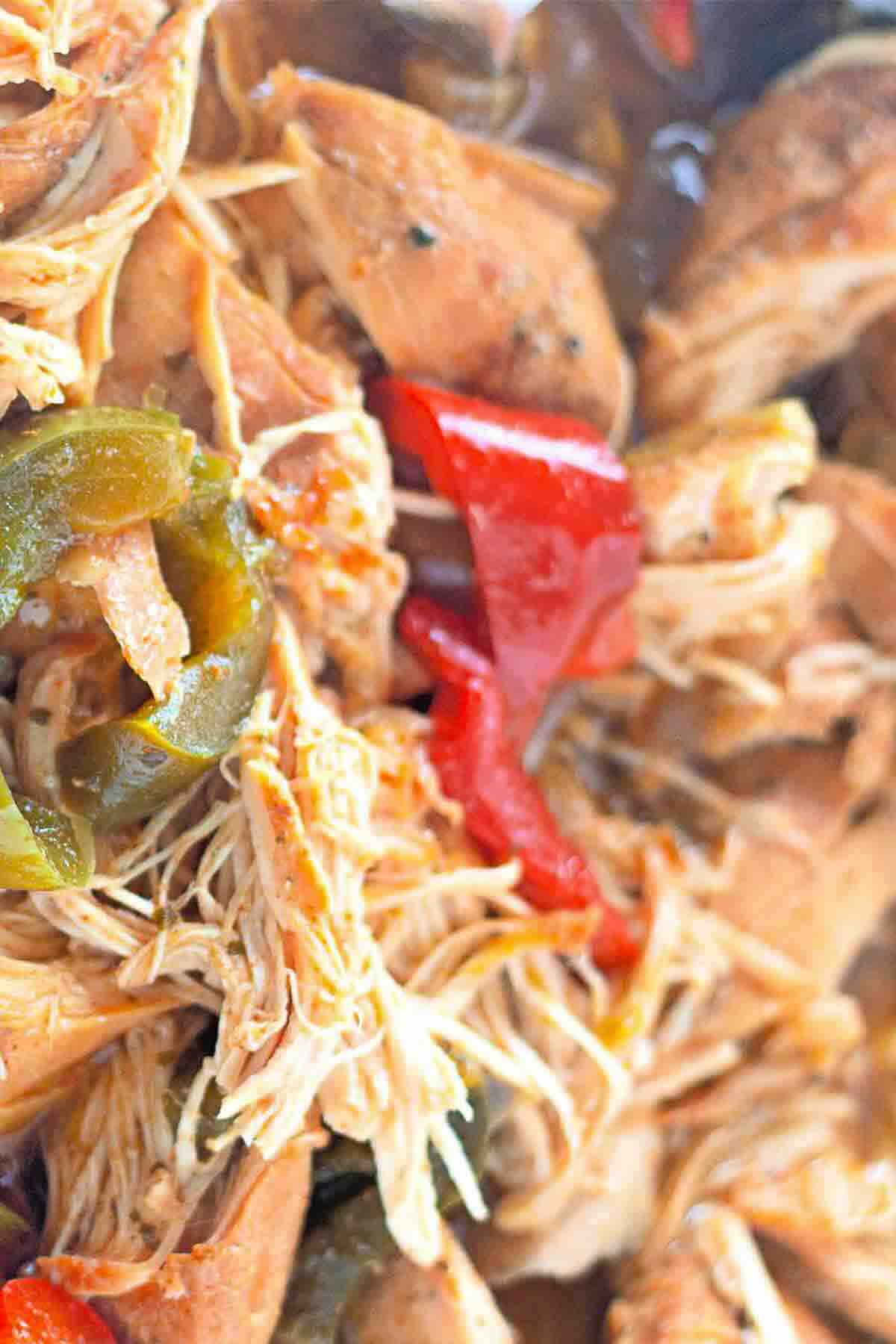 Close-up of shredded cooked chicken mixed with sliced red and green peppers.