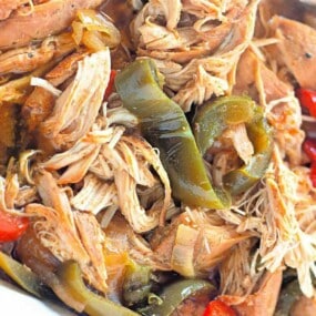 Close-up of shredded cooked chicken mixed with sliced green and red bell peppers.