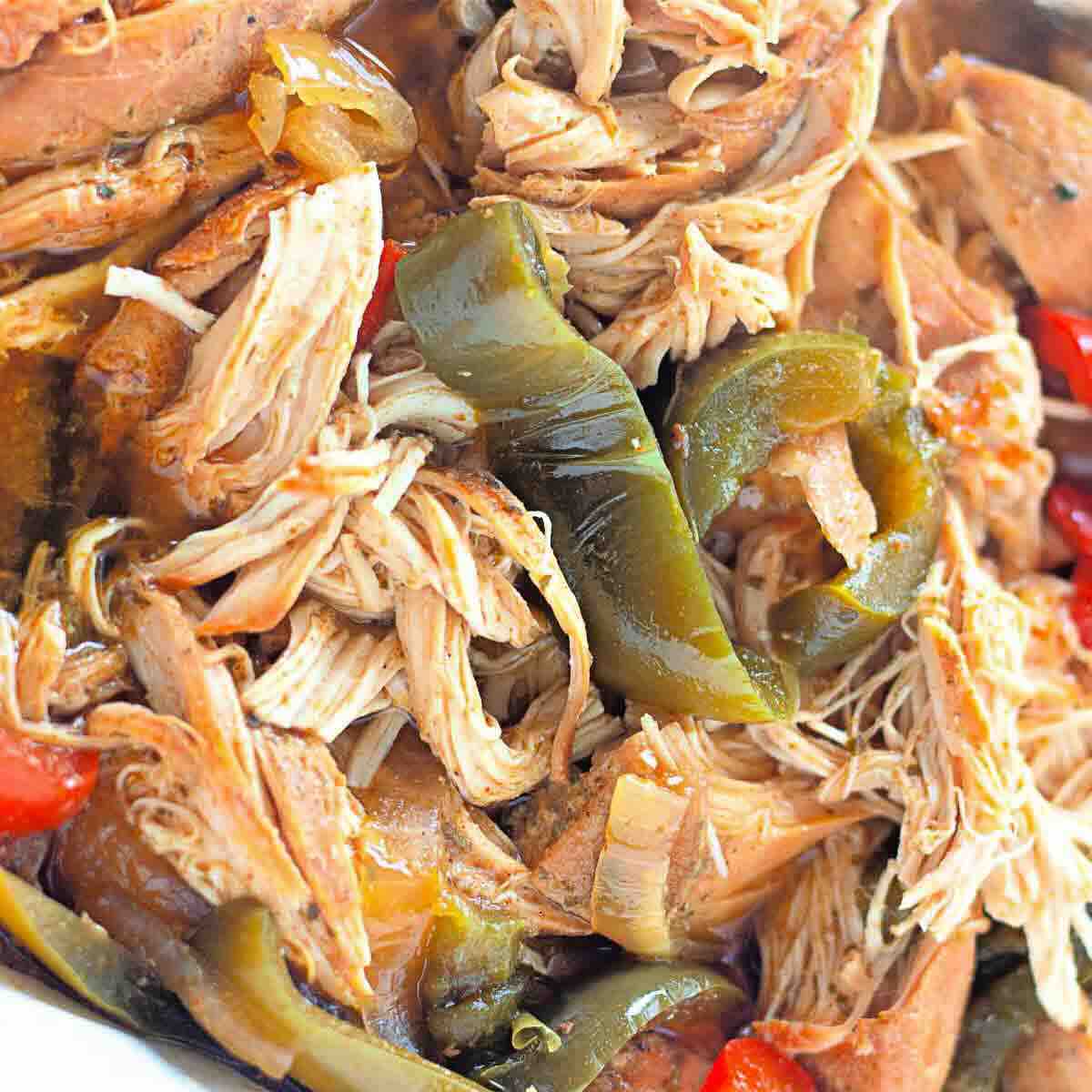 Close-up of shredded cooked chicken mixed with sliced green and red bell peppers.