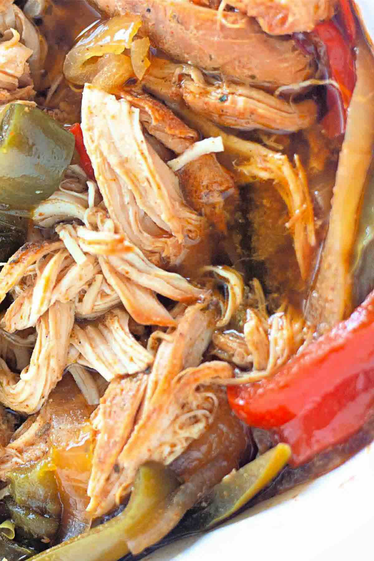 Shredded cooked chicken mixed with sliced red and green bell peppers in a brown sauce.