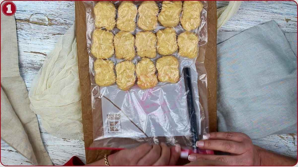 A person holds a vacuum sealer and a bag of arranged dough balls on a wooden surface, preparing to seal the bag.