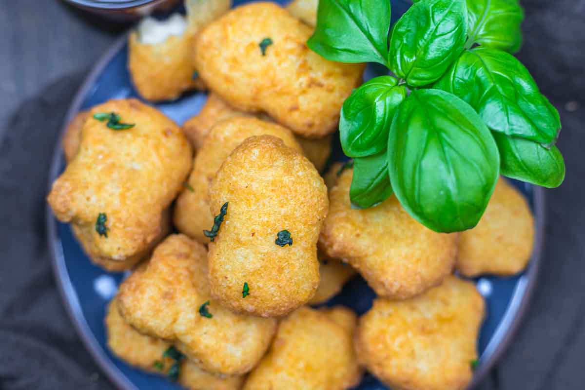 A plate of golden-brown, breaded nuggets garnished with fresh basil leaves.