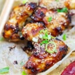 Close-up of grilled chicken wings topped with sesame seeds and chopped green onions on parchment paper.