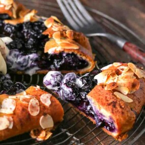 A blueberry galette topped with sliced almonds and a scoop of ice cream sits on a wire rack with a fork beside it.
