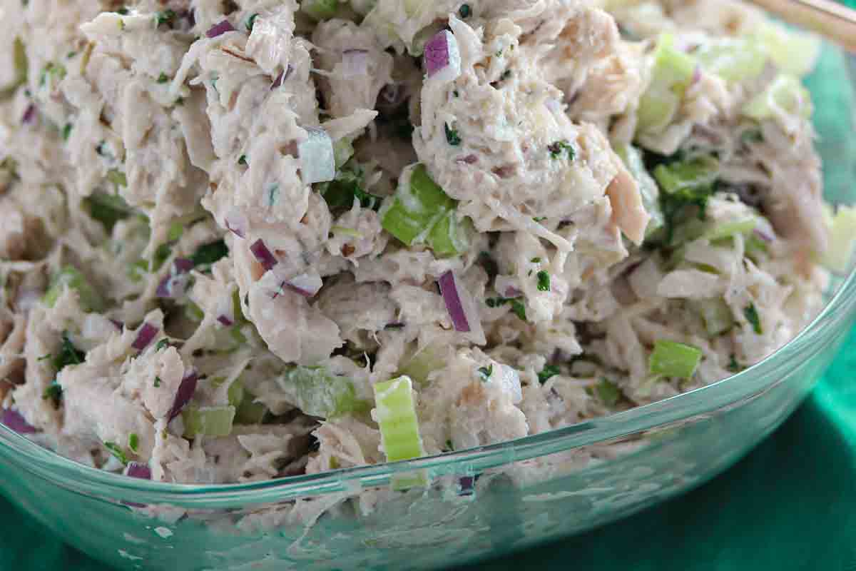 A close-up of chicken salad with chopped celery, red onion, and herbs in a glass container.