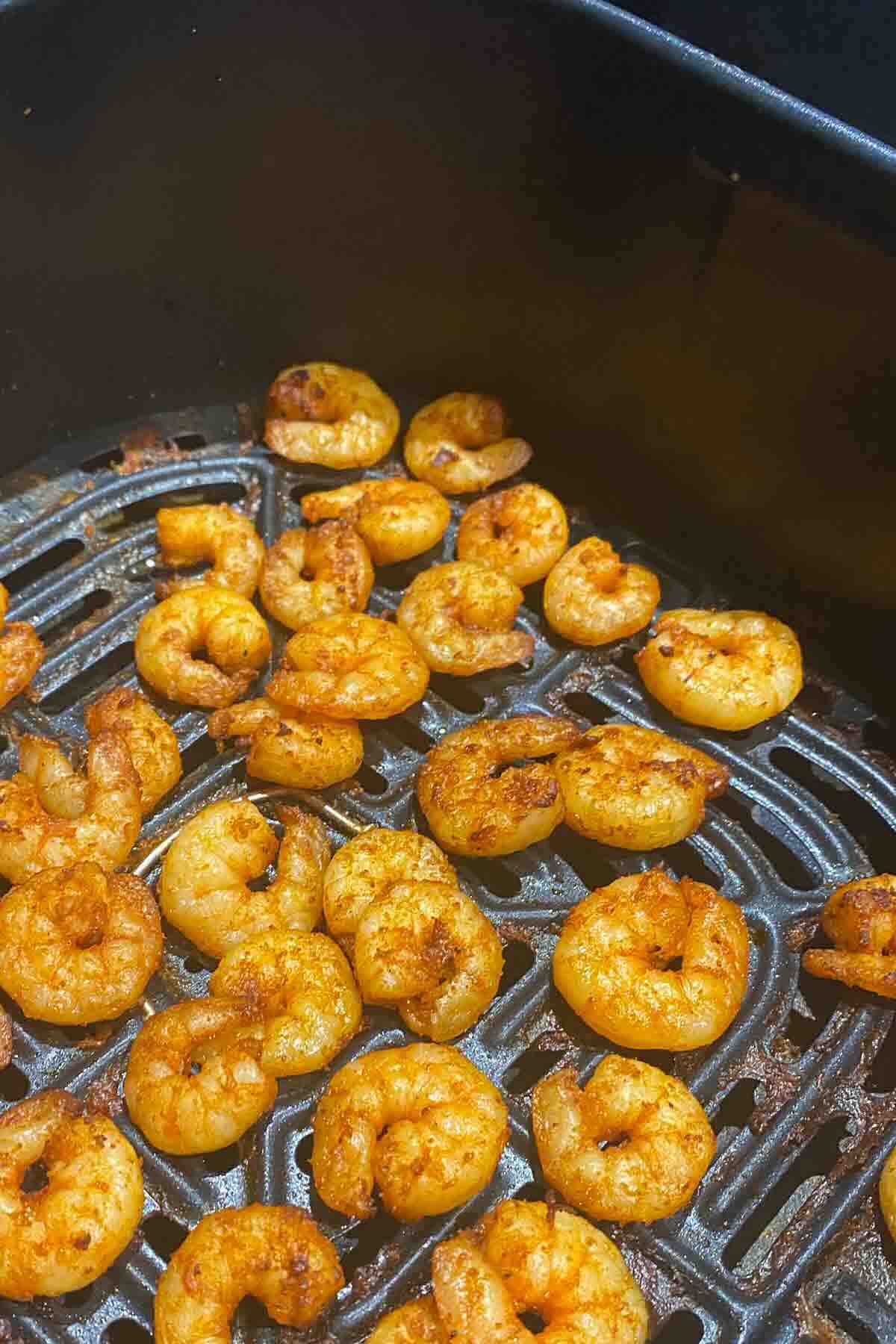 Seasoned shrimp cooking in an air fryer basket, arranged evenly on the grill tray.