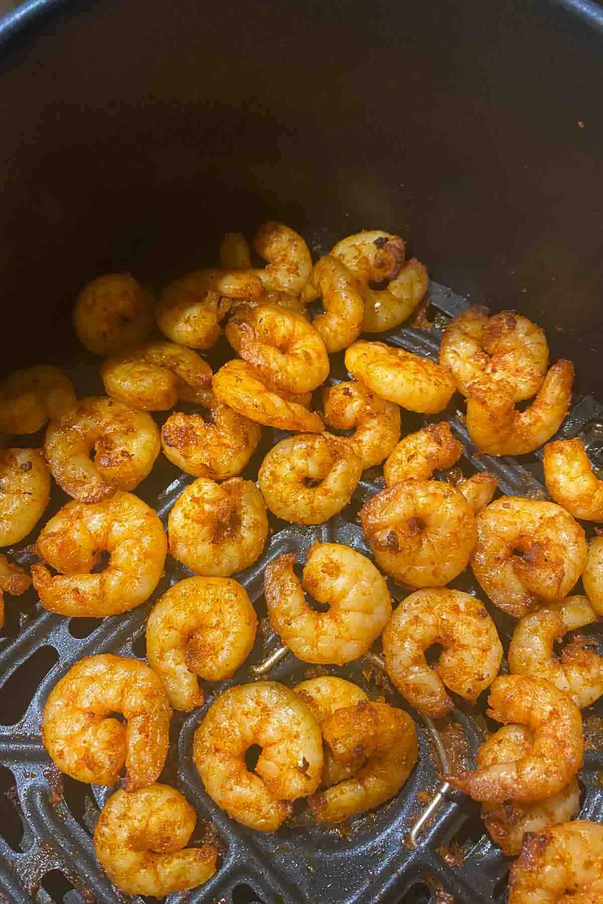 Seasoned shrimp cooking in an air fryer basket.