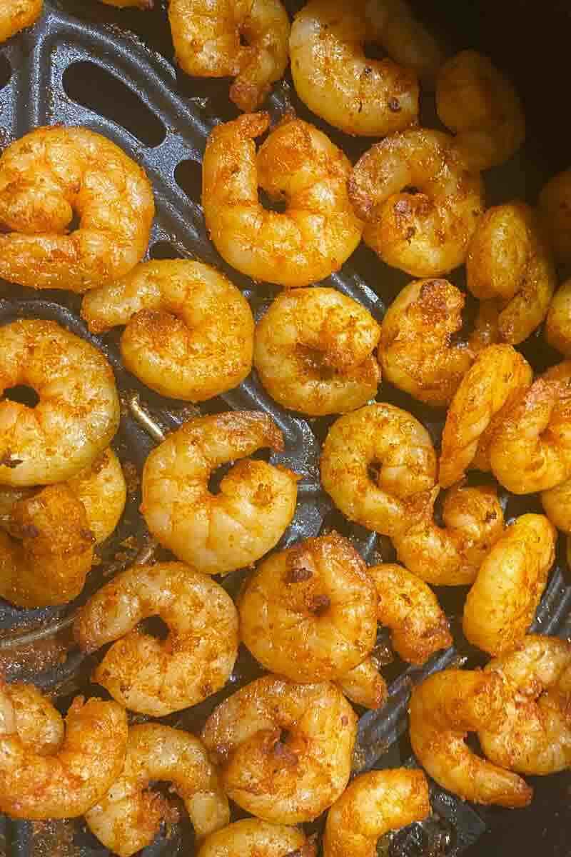 Seasoned shrimp cooking in an air fryer basket, displaying a golden-brown color and slightly crispy texture.