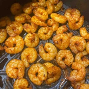 Cooked, seasoned shrimp arranged on an air fryer tray.