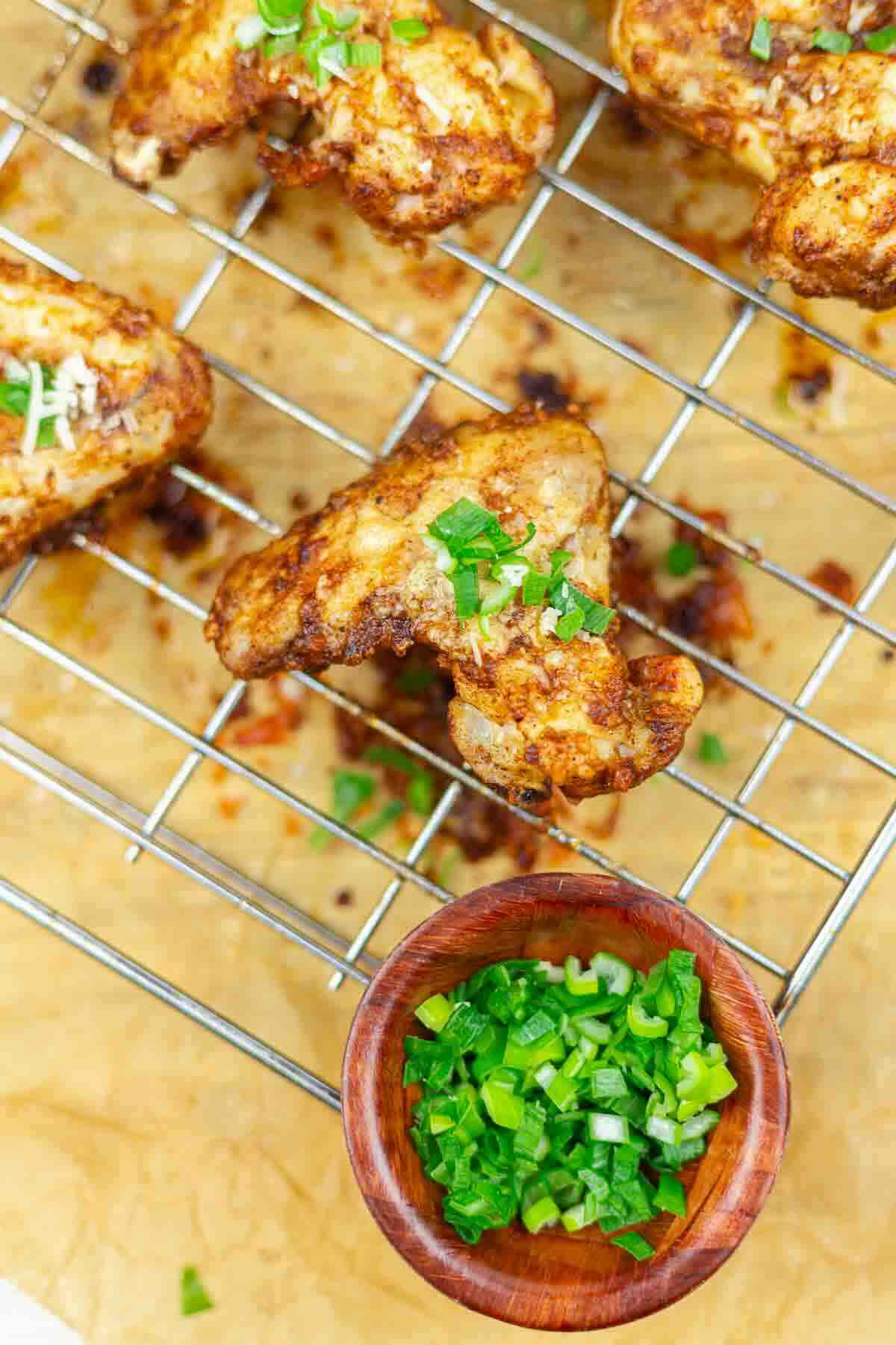 Grilled chicken wings on a wire rack lined with parchment paper, garnished with chopped green onions, with a small bowl of green onions nearby.