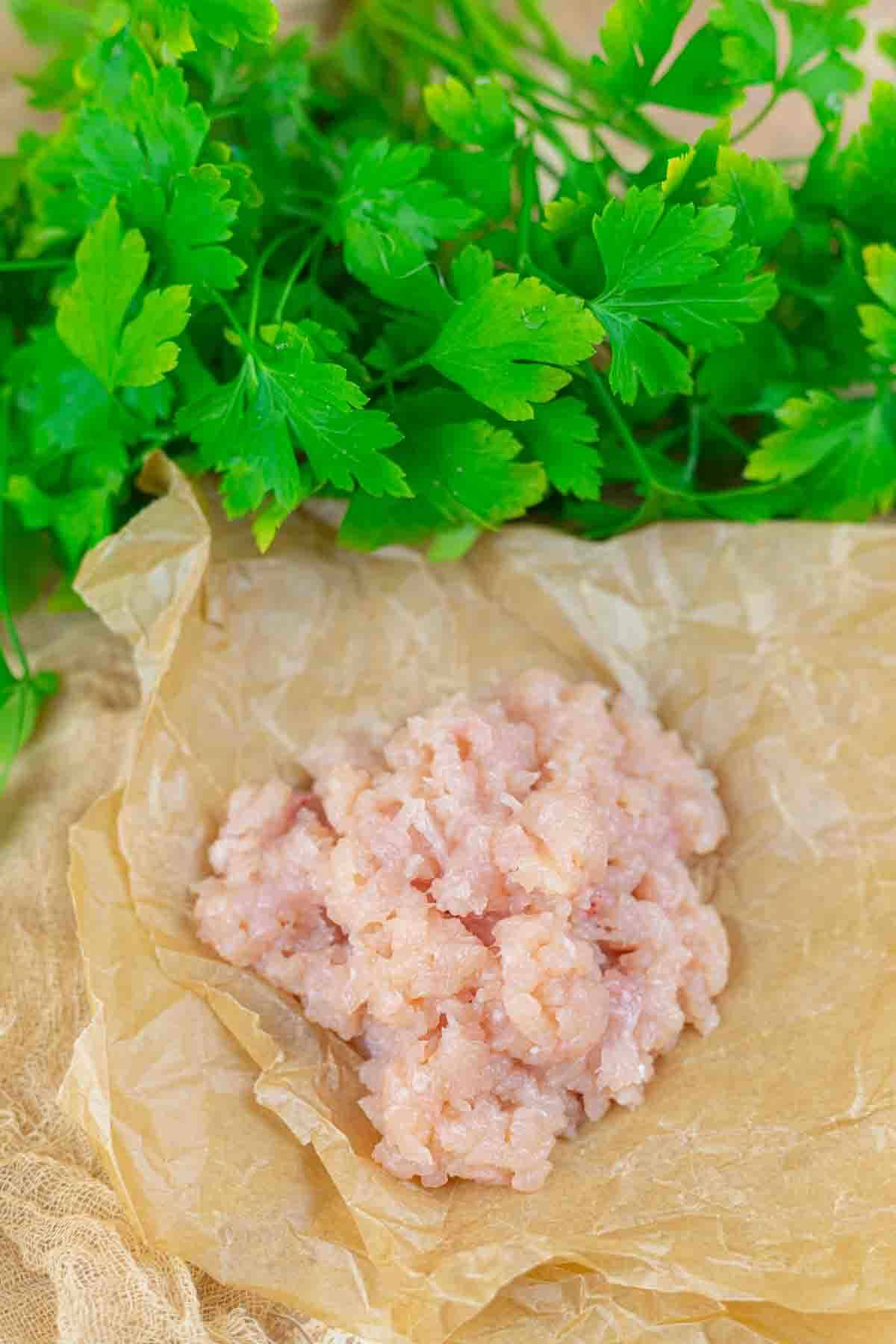 Raw ground chicken placed on a piece of parchment paper with fresh parsley in the background.
