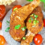 Two pieces of breaded, fried chicken garnished with chopped green onions on a plate, surrounded by cherry tomatoes.
