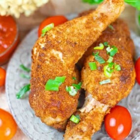 Two pieces of breaded, fried chicken garnished with chopped green onions on a plate, surrounded by cherry tomatoes.