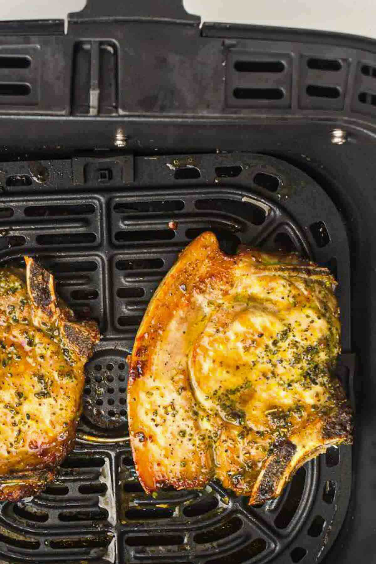Two seasoned pork chops cooking inside a black air fryer basket.