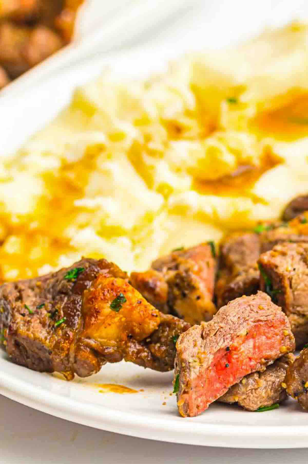 A close-up of a plate with sliced steak bites and mashed potatoes topped with brown gravy.