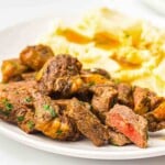 Plate with pieces of seasoned, cooked steak and a serving of mashed potatoes with gravy.