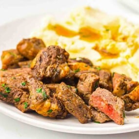Plate with pieces of seasoned, cooked steak and a serving of mashed potatoes with gravy.