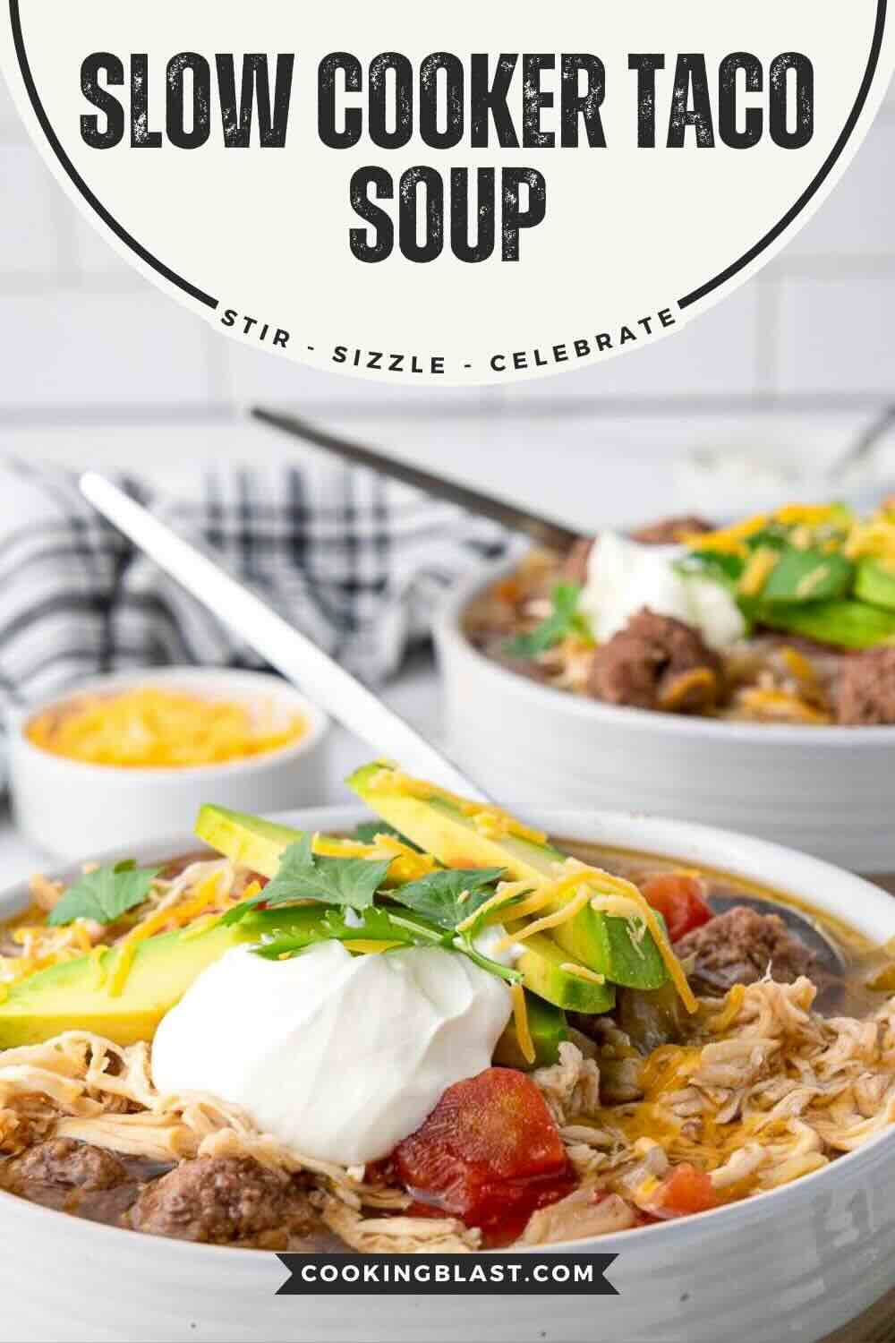 A bowl of slow cooker taco soup topped with avocado slices, sour cream, shredded cheese, and cilantro, with another bowl and a napkin in the background.