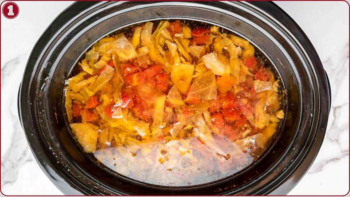 Overhead view of a slow cooker filled with chopped vegetables and liquid on a white countertop.