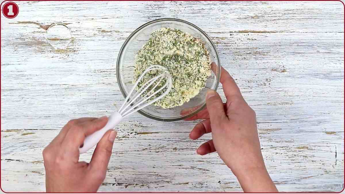 A person holding a bowl and whisk, mixing dry ingredients on a white wooden surface.