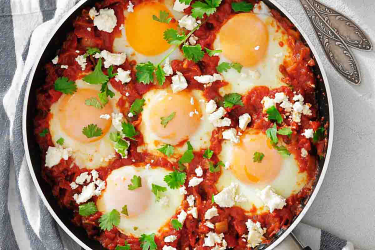 A skillet of shakshuka with poached eggs in tomato sauce, topped with fresh parsley and crumbled feta cheese.