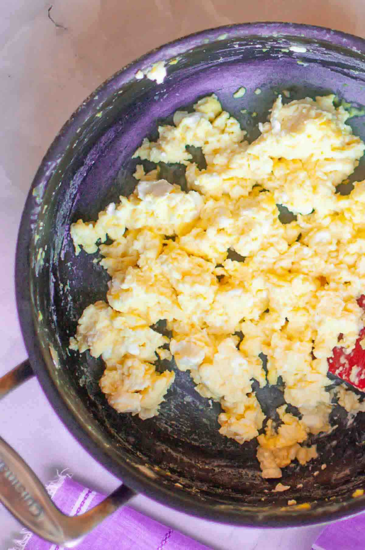 A close-up of scrambled eggs cooking in a black nonstick pan on a stove.
