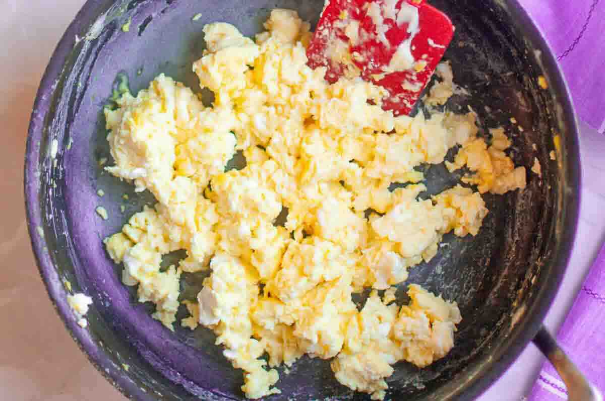 A close-up of scrambled eggs being cooked in a pan with a red spatula.