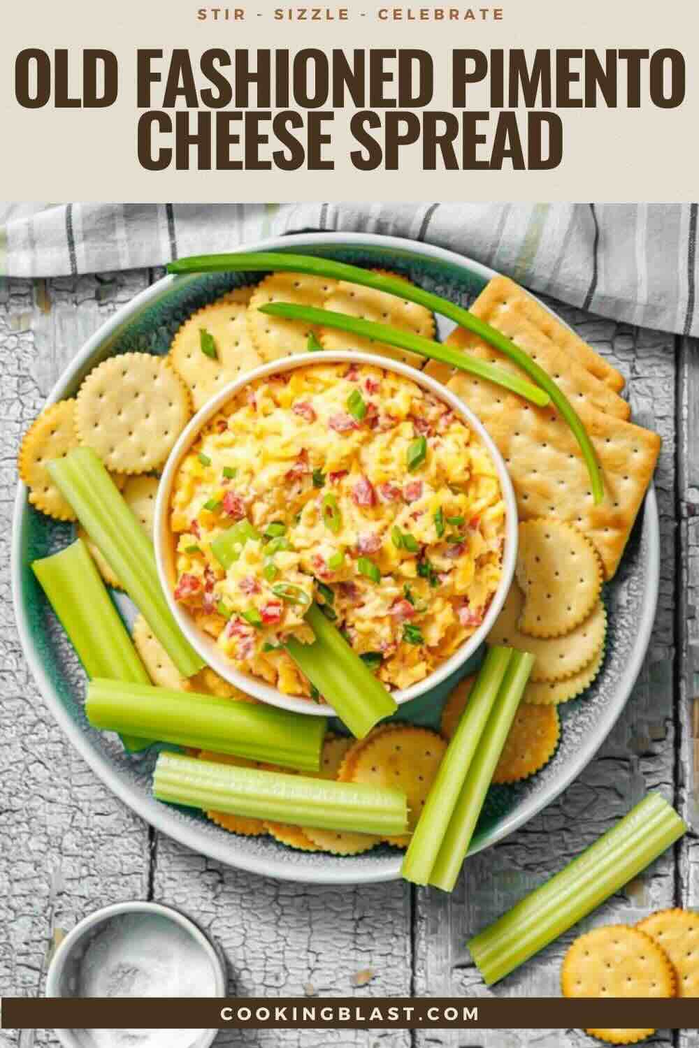 A bowl of pimento cheese spread is surrounded by celery sticks and assorted round crackers on a plate, atop a rustic wooden surface.