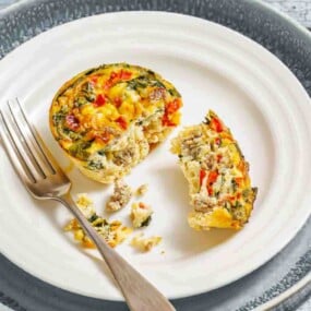 Mini quiche with vegetables and sausage, cut in half on a white plate with a fork.