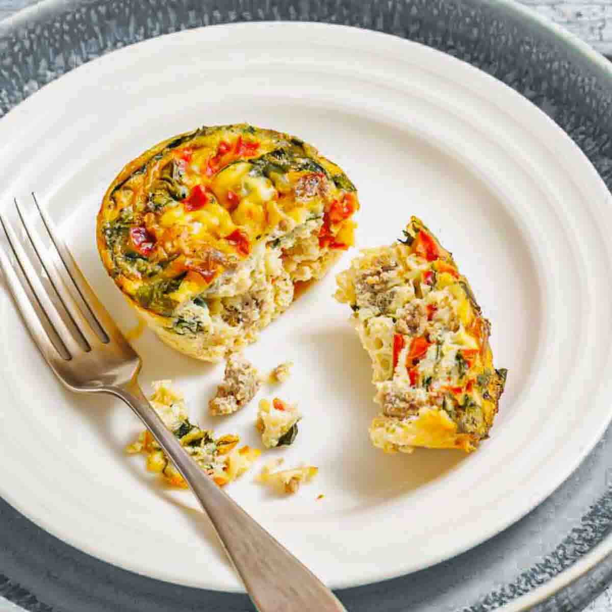 Mini quiche with vegetables and sausage, cut in half on a white plate with a fork.
