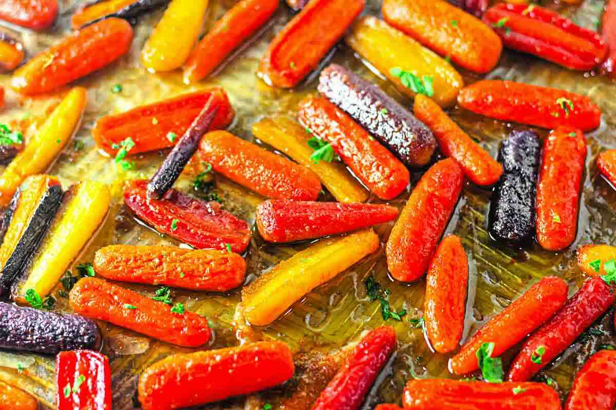 Close-up of roasted baby carrots in various colors on a baking sheet, garnished with chopped herbs and drizzled with oil.