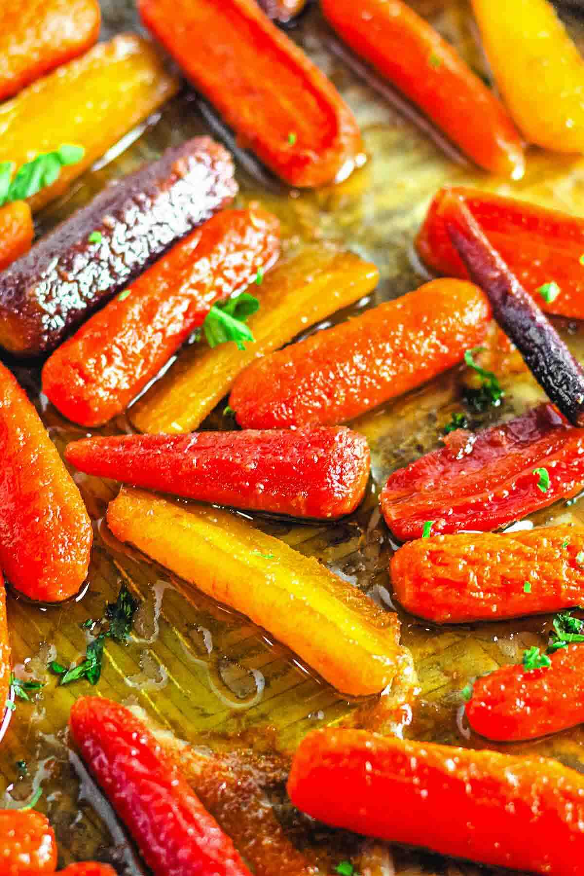 Colorful roasted baby carrots glazed in oil and garnished with herbs on a baking sheet.