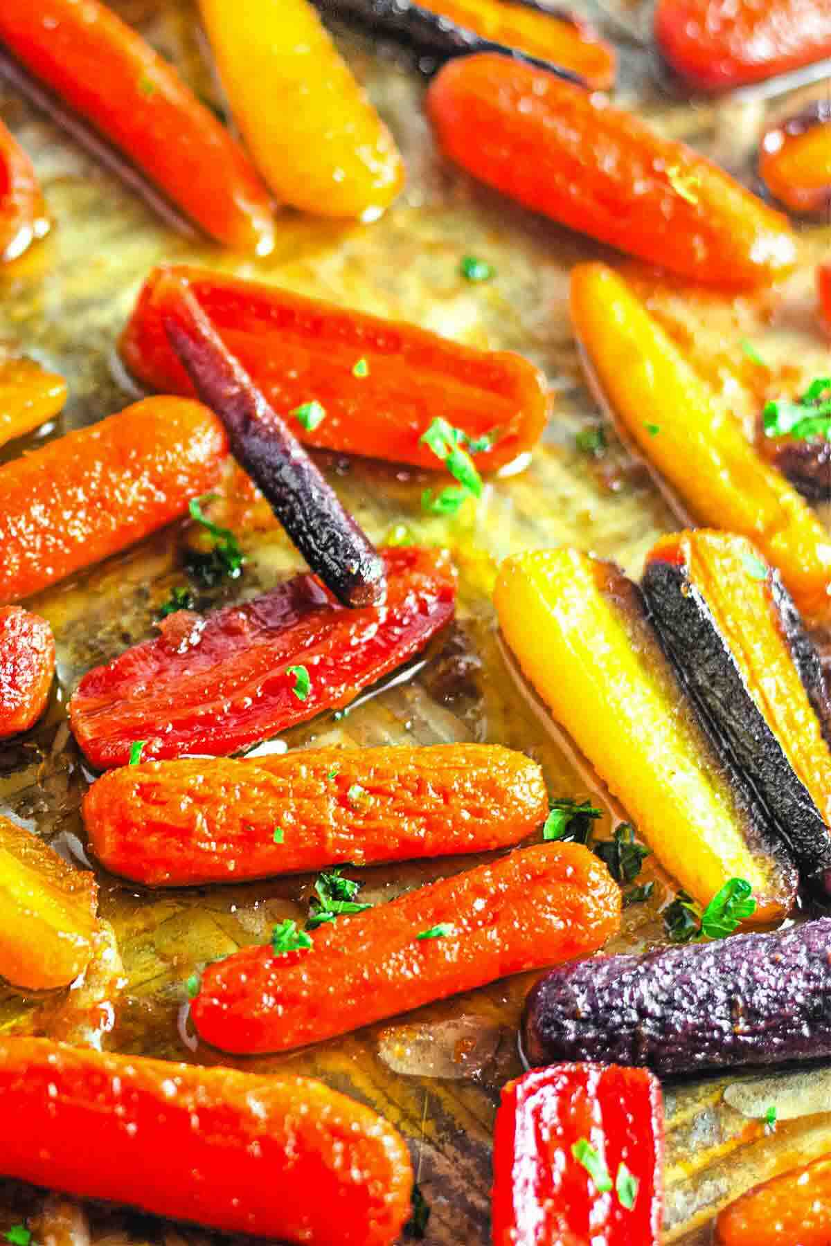 Close-up of roasted multicolored baby carrots on a baking sheet, garnished with chopped parsley.
