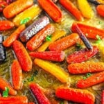 Roasted multicolored baby carrots coated in oil and garnished with chopped herbs on a baking sheet.