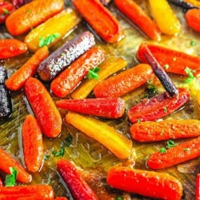 Roasted multicolored baby carrots coated in oil and garnished with chopped herbs on a baking sheet.