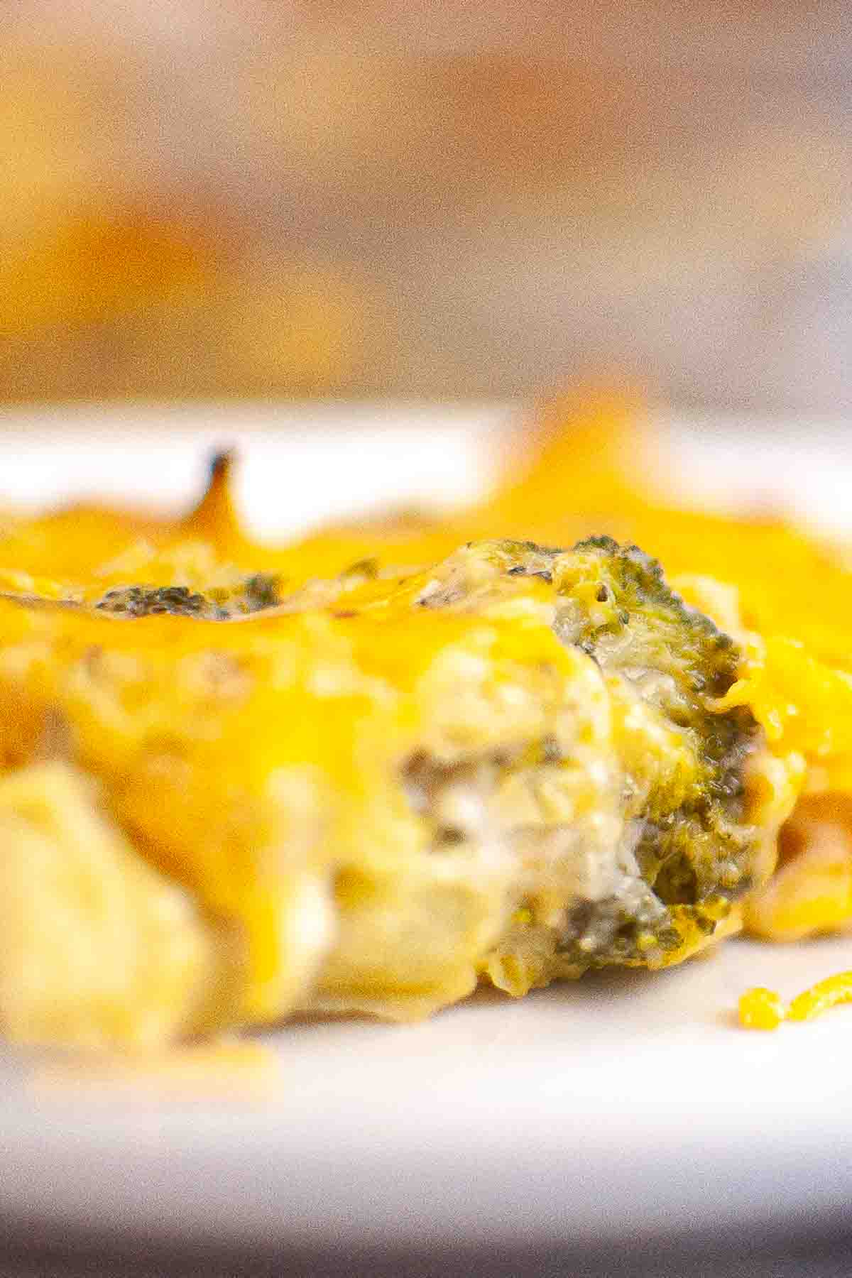Close-up of a cheesy casserole featuring broccoli and melted cheddar cheese on a white plate.